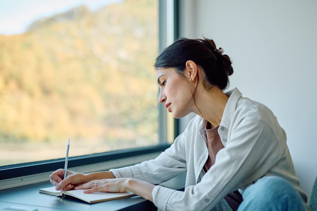 A woman writing in a notebook beside a window